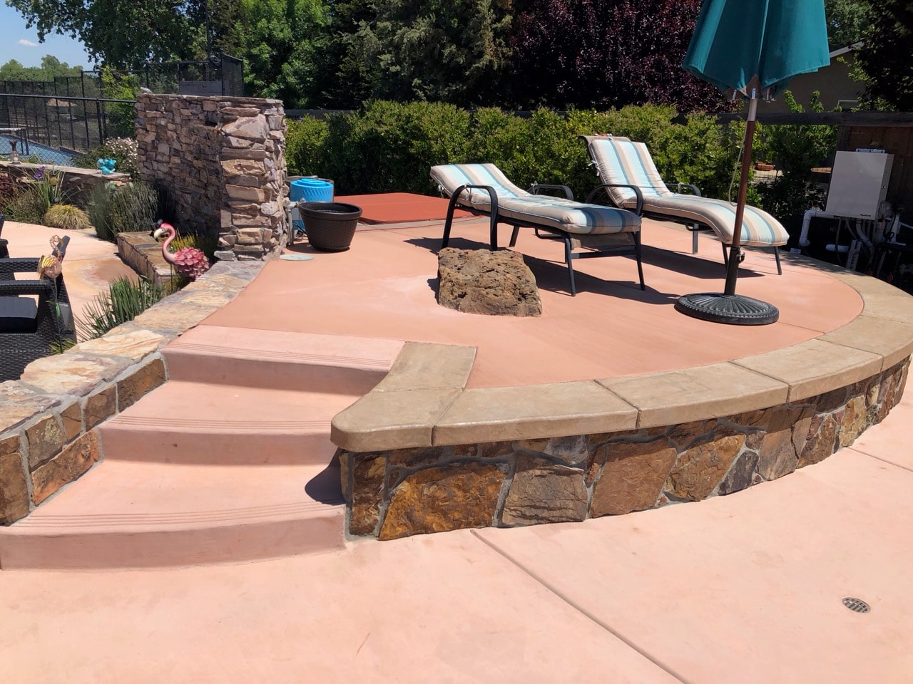 Outdoor concrete patio with stone seating wall and pool area by Capps Construction