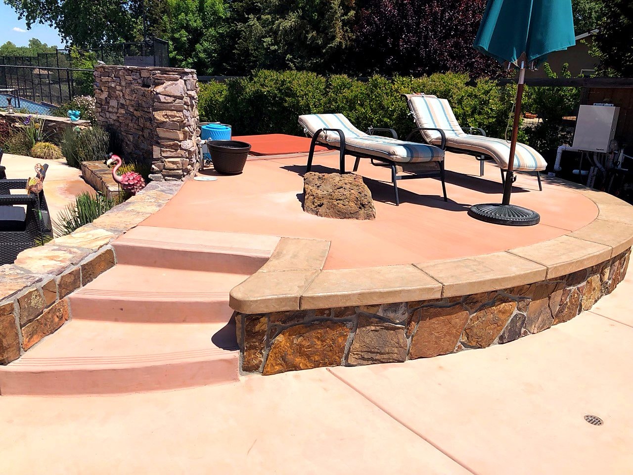Colored concrete patio with curved stone seat wall and steps by Capps Construction