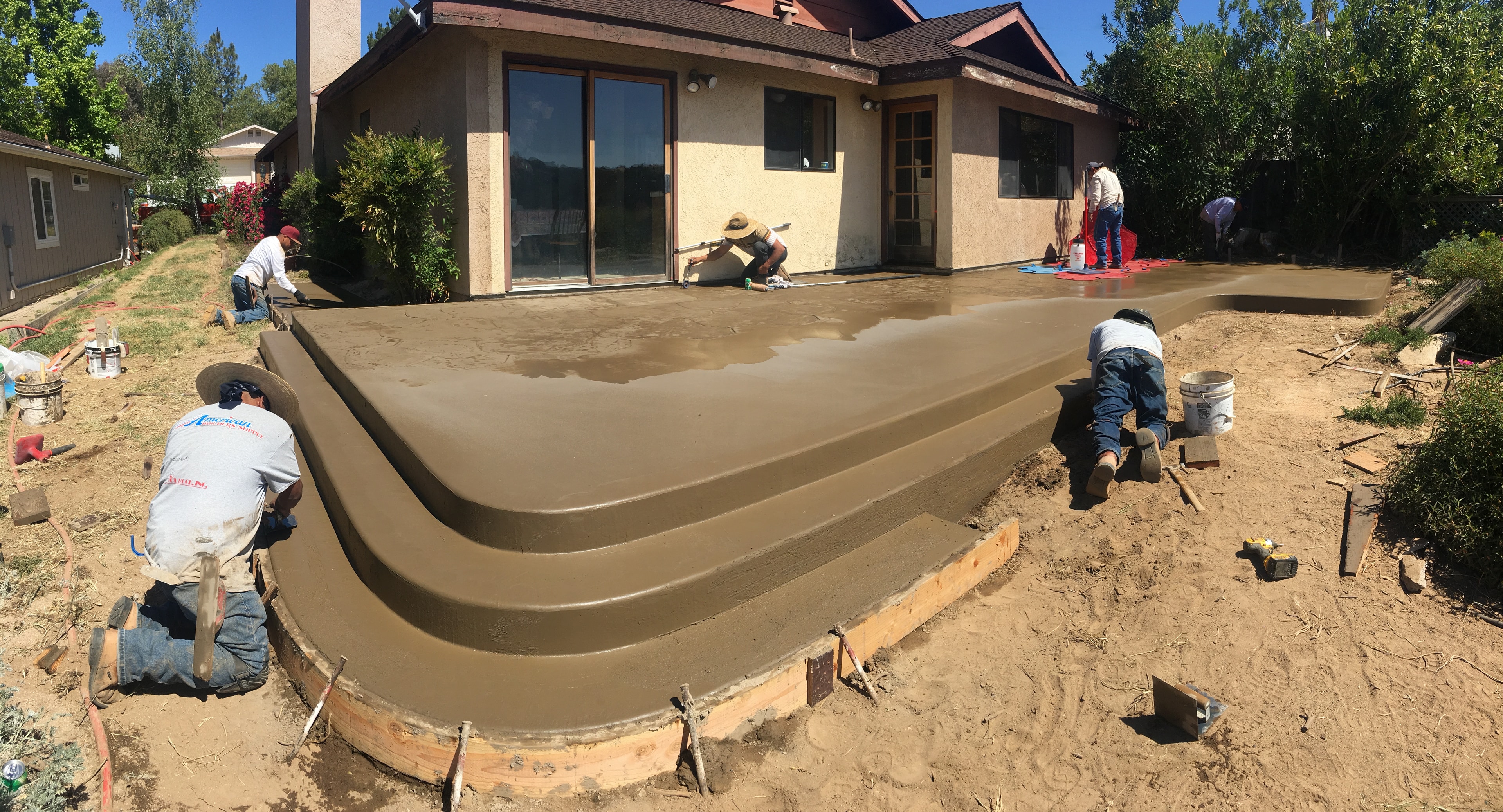 Workers pouring and finishing a concrete patio with curved steps